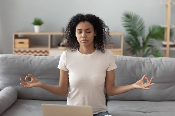 istock Focused black woman meditating on sofa at home 1179938863