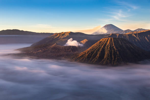 istock Mount Bromo at sunrise; East Java, Indonesia. Clouds cover the valley. White gas rising from crater. Blue sky above. 1179940588