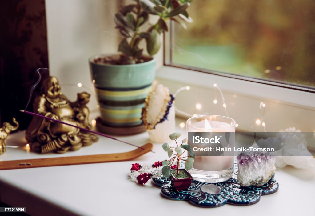 Feng Shui altar at home in living room or bed room. Attracting wealth and prosperity concept. Crystal clusters, wire tree with gemstones, golden smiling Buddha figure on table window sill. Domestic Life Stock Photo