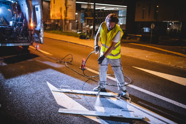 Nighttime Pavement Marking Crew Spray Painting Turn Arrow Construction crew member concentrating on spray painting new turn arrow in Central European capital city street. freshly painted road markings stock pictures, royalty-free photos & images