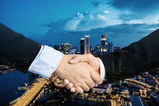 double exposure, cooperation or partnership business shaking hand with partnership after making profitable agreement with singapore city in background. Smart man handshake, deal and greeting concept.