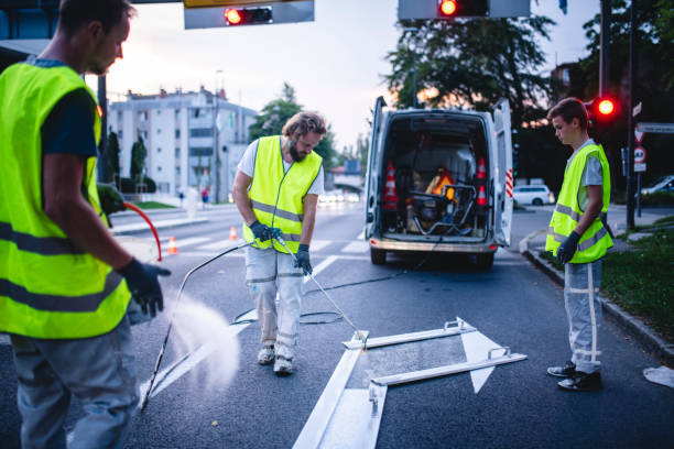 Construction Crew Member Spray Painting Turn Arrow at Dusk Three-man construction crew in reflective vests spray painting turn arrow marking in Central European capital city. freshly painted road markings stock pictures, royalty-free photos & images