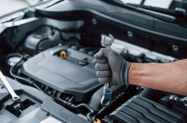 istock Everything will be fixed. Man's hand in glove holds wrench in front of broken automobile 1179949179