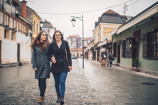 Two young Caucasian cute women walking along a city street together.