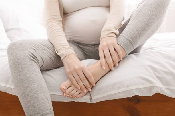 femme enceinte massant son pied gonflé s'asseyant sur le lit - abdomen women massaging human hand photos et images de collection