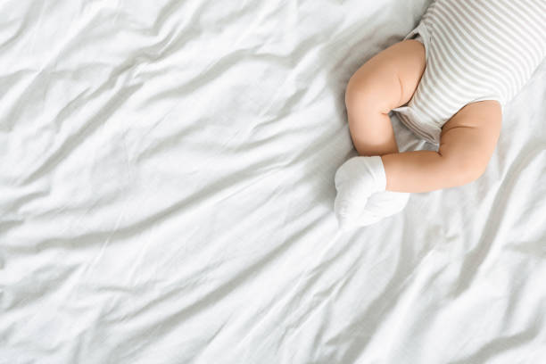 Top view of crossed legs of newborn baby Top view of crossed legs of newborn baby lying on bed in bodysuit and socks, panorama with free space ass boy stock pictures, royalty-free photos & images