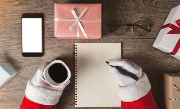 Santa Claus hands is writing something in a blank notebook.