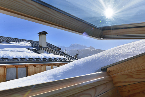 view from an opening window on a roof covering with snow in an alpine cottage