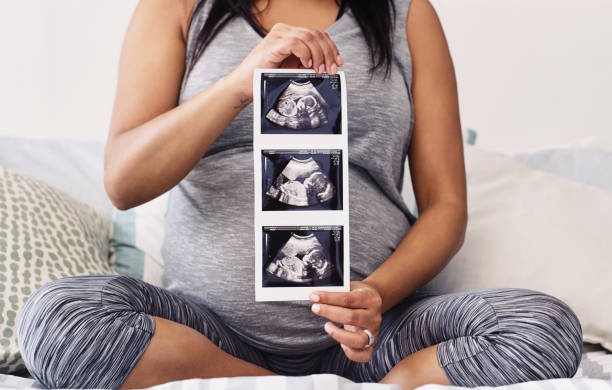 This is the first picture of my bundle of joy Shot of an unrecognizable woman holding her unborn child's sonogram at home routine photos stock pictures, royalty-free photos & images