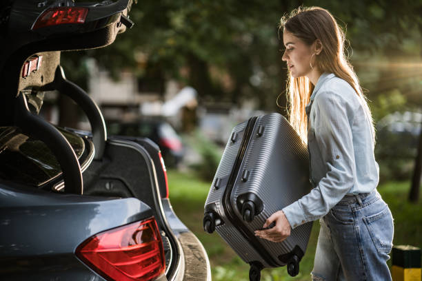Young woman packing her suitcase into the car trunk.