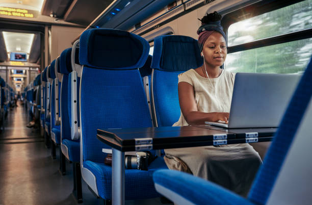 Music helps me get through my emails Cropped shot of an attractive young woman sitting and wearing earphones while using her laptop in the train travel destinations 20s adult adventure stock pictures, royalty-free photos & images