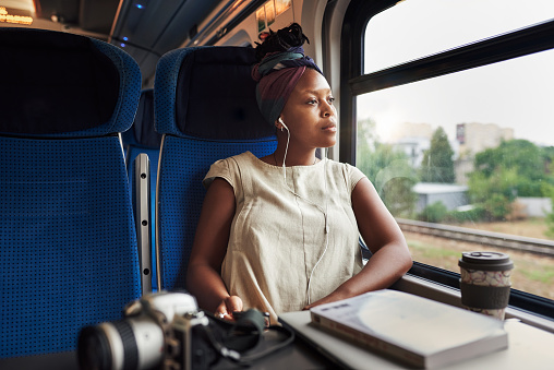 Cropped shot of an attractive young woman sitting alone in a train and looking contemplative while wearing earphones