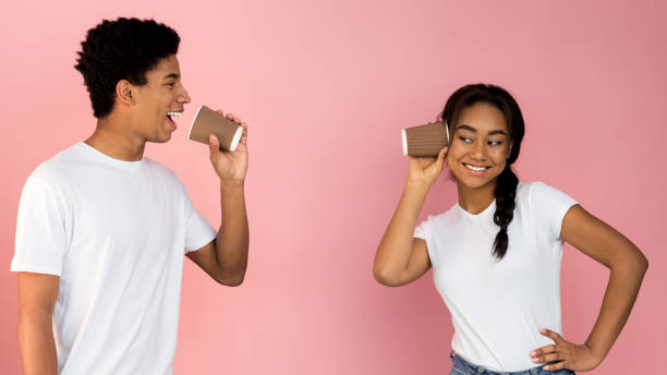 Loving teen couple talking through tin can phone Loving teen couple talking through tin can phone over pink background, panorama string telephone stock pictures, royalty-free photos & images