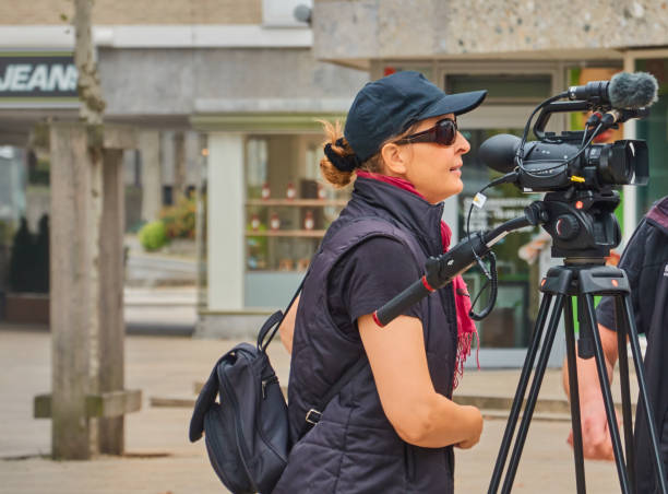 jeune camerawoman avec l'équipement vidéo professionnel léger sur un trépied, des lunettes de soleil et la casquette noire tire un film. - photographer camera tripod paparazzi photographer photos et images de collection