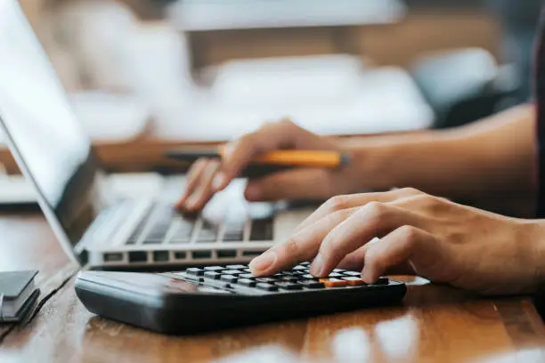 Photo of Close up man hands using a calculator and laptop computer for calculating with finance paper, tax, accounting, Accountant concept.