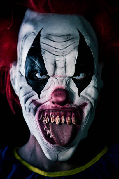 scary evil clown sticking out his tongue closeup of a scary evil clown with red hair, white eyes, bloody teeth, sticking out his tongue staring at the observer with a threatening look face paint halloween adult men stock pictures, royalty-free photos & images