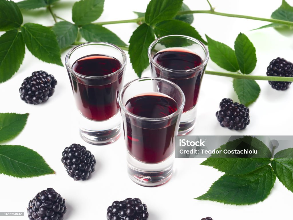 Three glasses of blackberry liqueur, also known as creme de mure Three glasses of blackberry liqueur, also known as creme de mure, on white background, decorated with bramble sprigs and fresh blackberries Blackberry - Fruit Stock Photo