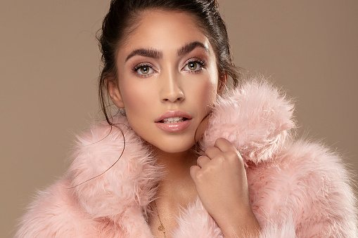 Beauty portrait of elegant young brunette girl wearing pink eco fur, looking at camera. Attractive woman in delicate glamour makeup.
