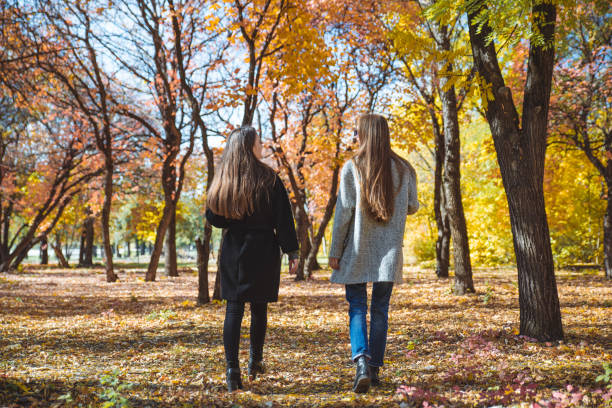 istock two girlfriends walking by autumn city park talking 1179963932