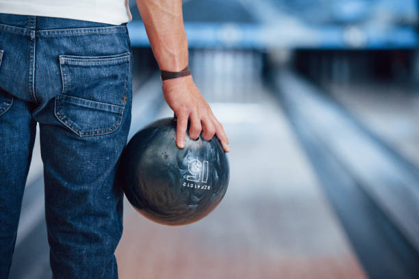 iluminação artificial. opinião traseira da partícula do homem na roupa ocasional que joga o bowling no clube - bowling holding bowling ball hobbies - fotografias e filmes do acervo