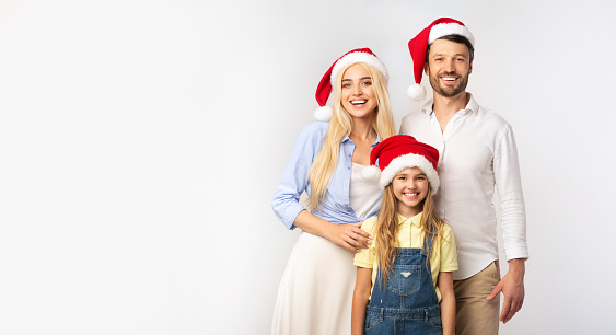 Christmas Holidays. Family Of Three In Santa Hats Standing And Smiling On White Background In Studio. Isolated