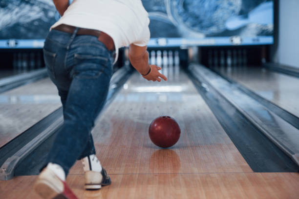 los geht es. rückansicht des mannes in lässiger kleidung beim bowling im club - bowling holding bowling ball hobbies stock-fotos und bilder