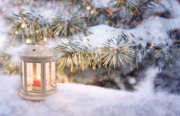 istock Christmas lantern with burning candle shines on snow and spruce branches, snowfall winter scene with light and bokeh 1179965958