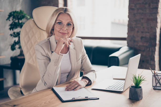 Photo of happy cheerful professional qualified teacher listening to her student during seminar at business holding pen with her hand wearing spectacles Photo of happy cheerful professional qualified teacher listening to her student during seminar at business, holding pen with her hand wearing spectacles qualified report stock pictures, royalty-free photos & images