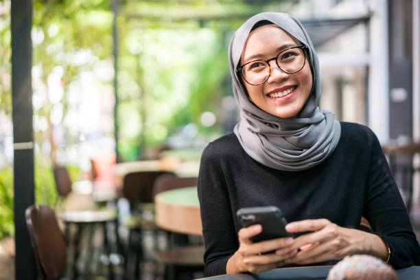 Cheerful Malaysian businesswoman in a cafe Cheerful Malaysian businesswoman using her smartphone in a cafe. scarf photos stock pictures, royalty-free photos & images
