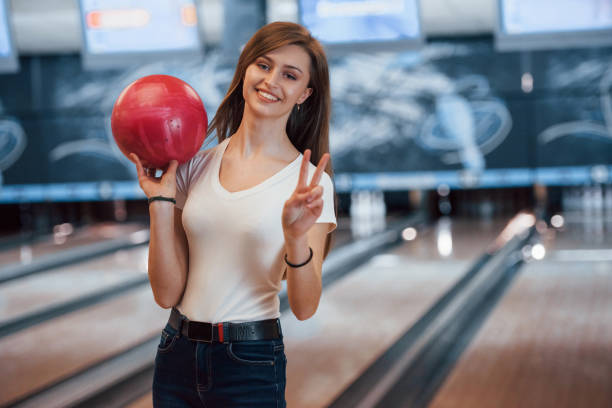 クラブで赤いボウリングボールを持つカジュアルな服を着た陽気な若い女性 - bowling holding bowling ball hobbies ストックフォトと画像