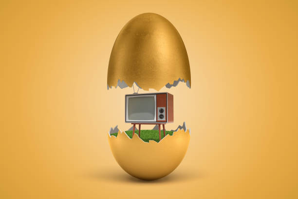 istock 3d rendering of gold egg cracked in two, upper half levitating in air, retro TV set standing on green grass inside lower half, on ocher background. 1179971454