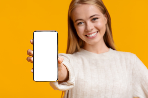 App for education. Cute teenage girl showing blank smartphone screen over orange background with empty space.