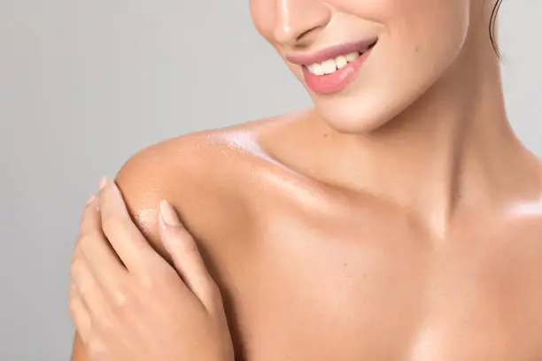 Close up studio shot of a beautiful woman with perfect skin, she applying cream at her shoulder