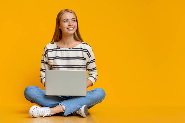 adolescente chica sentada con la computadora portátil en el suelo y mirando a un lado - con las piernas cruzadas fotografías e imágenes de stock