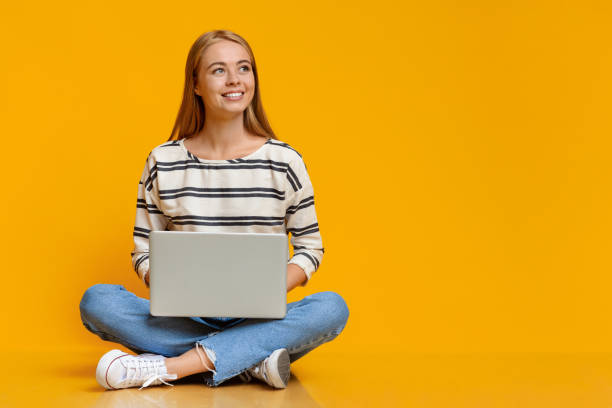 teenage girl sitting with laptop on floor and looking aside - aside imagens e fotografias de stock