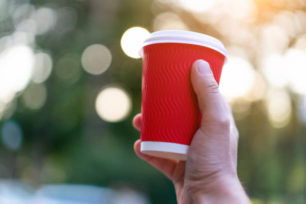 istock Red paper cup for drinks in hand on a background of nature. 1179989621