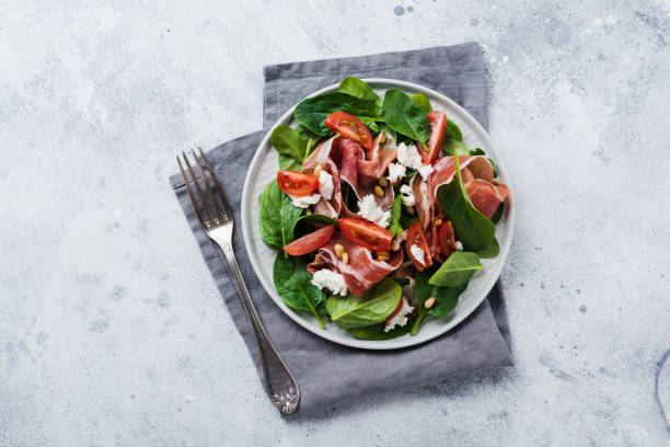 istock Spring Salad with spinach, cherry tomato, mozzarella, pine nuts and ham with olive oil in a simple ceramic plate on an old concrete gray background. 1179991317