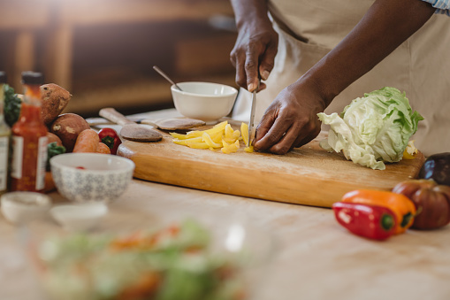 Cropped closeup of an African American woman standing at a counter in her kitchen at home cutting up vegetables for a delicious salad