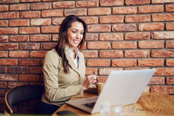 Focused smiling businesswoman dressed smart casual sitting in cafe, stirring coffee and looking at laptop. Focused smiling businesswoman dressed smart casual sitting in cafe, stirring coffee and looking at laptop. stirring stock pictures, royalty-free photos & images