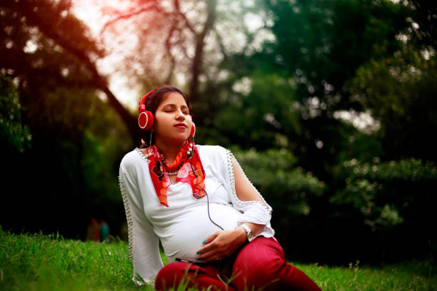 беременные женщины, наслаждающиеся музыкой на наушники в парке - new delhi audio стоковые фото и изображения