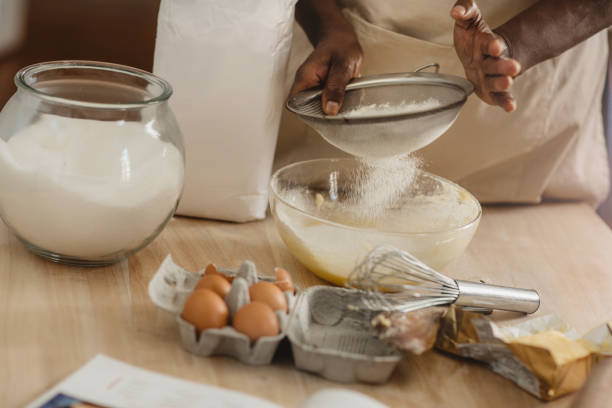 femme d'afro-américain tamisant la farine tout en cuisinant à la maison - sifting photos et images de collection