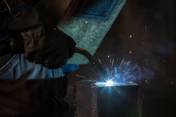 istock Worker in a protective wardrobe with a mask and gloves is welding a metal objects in a metal workshop. 1179994019