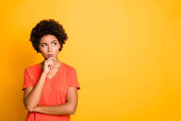 photo de copyspace de contempler regardant regardant la petite amie regardant regardant utilisant le t-shirt orange touchant son menton méditant au-dessus de quelque chose pour choisir l'isolement au-dessus du fond vif jaune de couleur - en désordre photos et images de collection