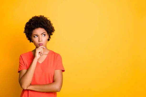 Copyspace photo of contemplating watching looking staring girlfriend wearing, orange t-shirt touching her chin pondering over something to choose isolated over yellow vivid color background