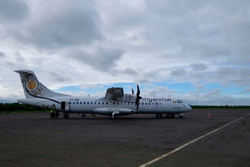 Mandalay/Myanmar-Sep. 2019: flank view of one propeller-driven plane of Myanmar Airways Corporation on ground at Mandalay International Airport. Cloudy blue skyline background