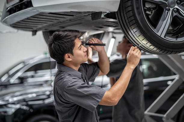 Asian mechanic Checking and torch tire in maintainance service center which is a part of showroom, technician or engineer professional work for customer, car repair concept stock photo