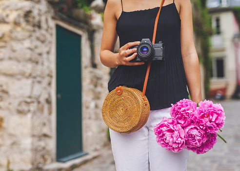 Shot of a woman holding a camera and a bunch of flower while out in the city