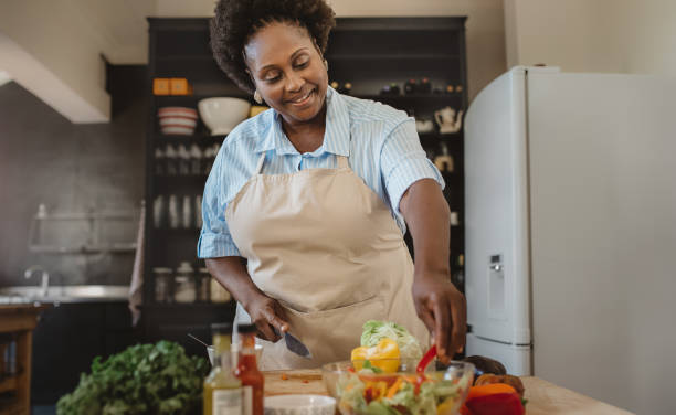 lächelnde afroamerikanische frau hackt gemüse in ihrer küche - dressing room women female adult stock-fotos und bilder
