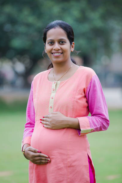 Smiling pregnant woman standing outdoor holding hands on belly stock photo Pregnant, Women, Females, south indian lady stock pictures, royalty-free photos & images