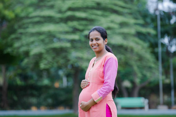Smiling pregnant woman standing outdoor holding hands on belly stock photo Pregnant, Women, Females, south indian lady stock pictures, royalty-free photos & images